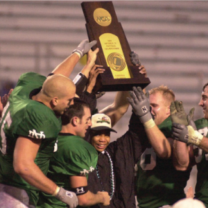 markus hoists trophy above head with football players surrounding him